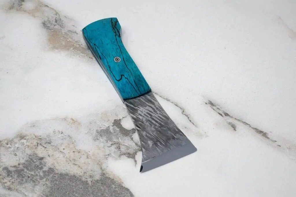 A Forged American Signature Classic knife, featuring a blue handle and grey blade, rests elegantly on a marble surface.